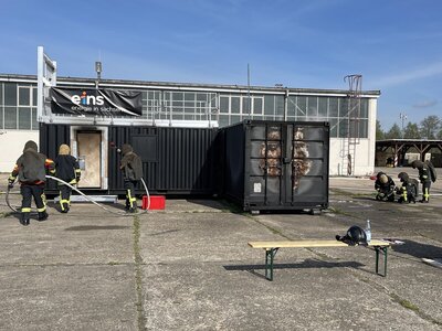 Kameradinnen und Kameraden üben an einem Feststoffbrandcontainer. Foto: eins